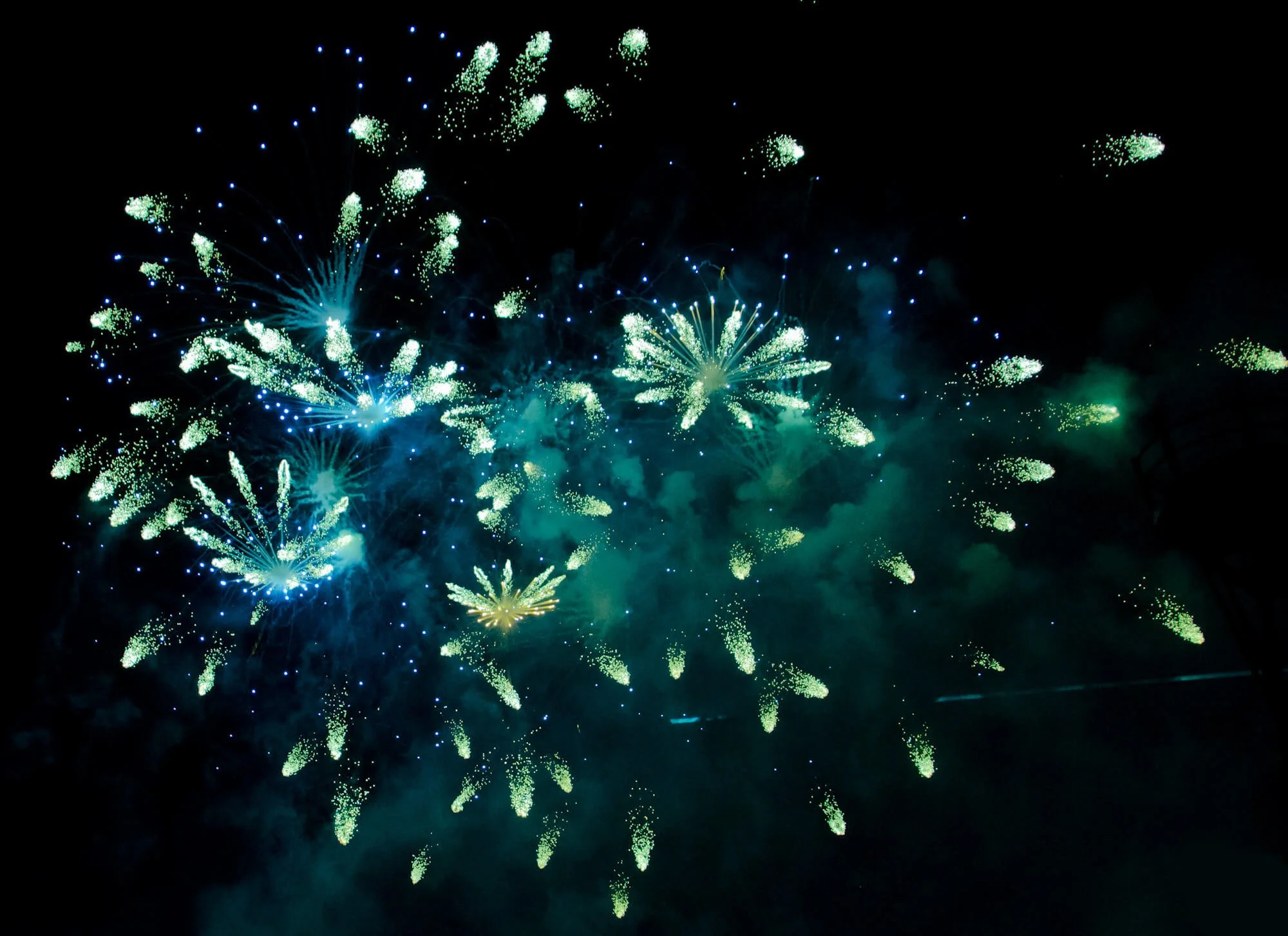 Colorful fireworks display against a dark night sky, with bursts of green and blue lights illuminating the scene.