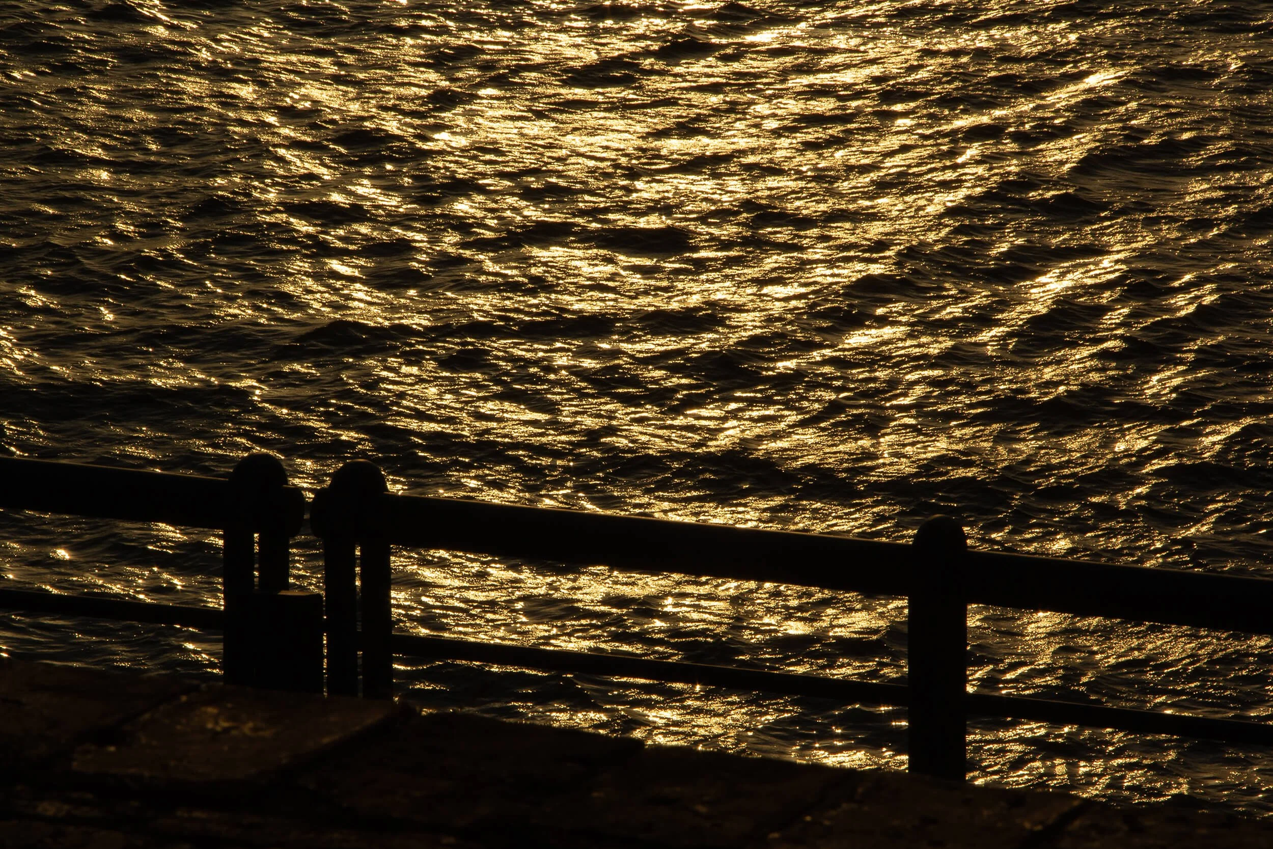 Sunset reflecting on the water surface near a pier or railing.