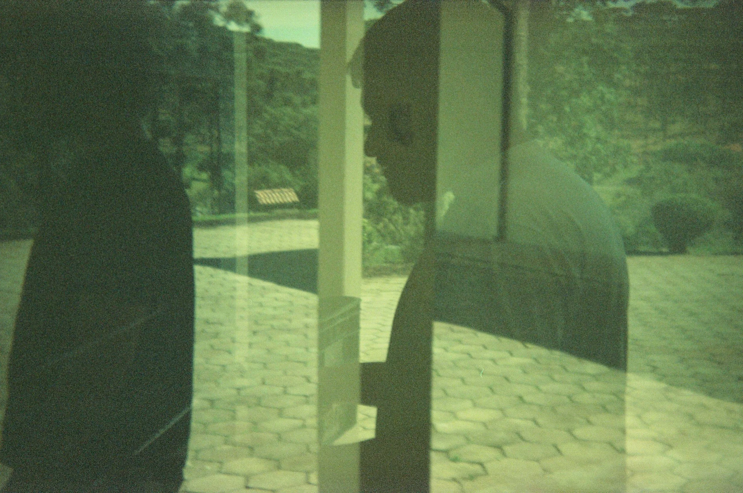 Reflection of two people standing outside a glass door, with trees and a brick walkway visible in the background.