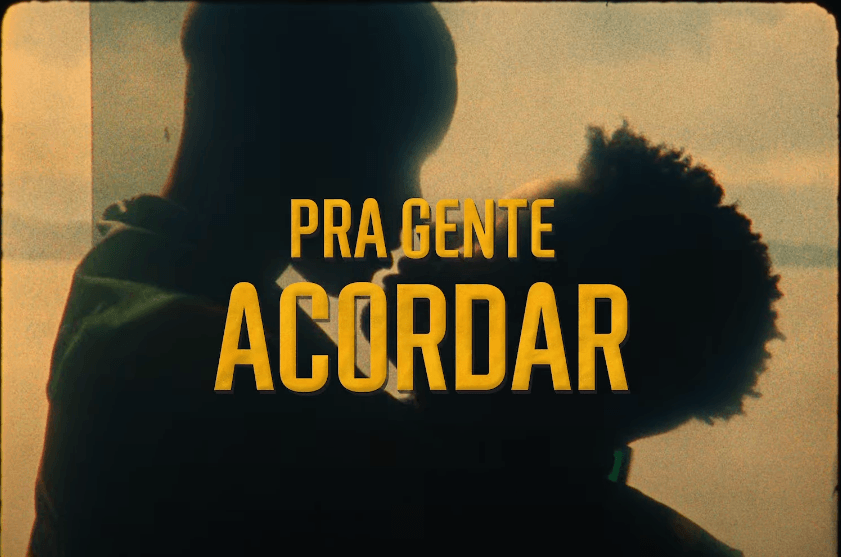 Silhouette of a couple close together, with the woman resting her head on the man's shoulder, against a sunset background. Overlaid text in Portuguese: "Pra Gente Acordar" in yellow.