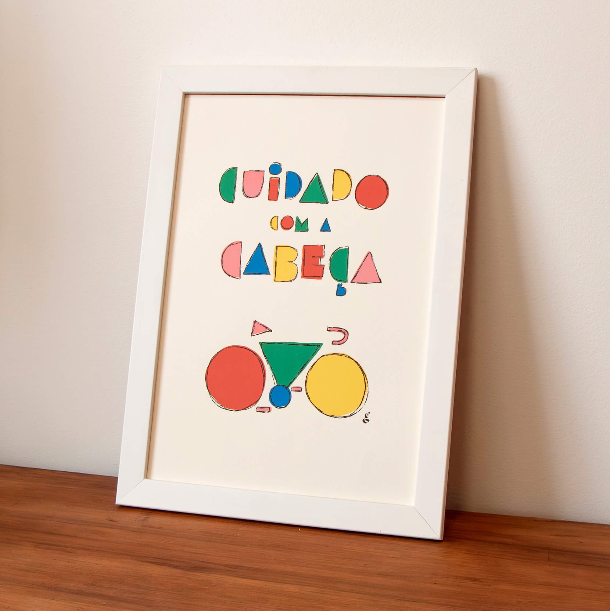 A framed colorful alphabet poster leaning against a wall on a wooden surface, with the word 'CUIDADO' written at the top and various geometric shapes in different colors.