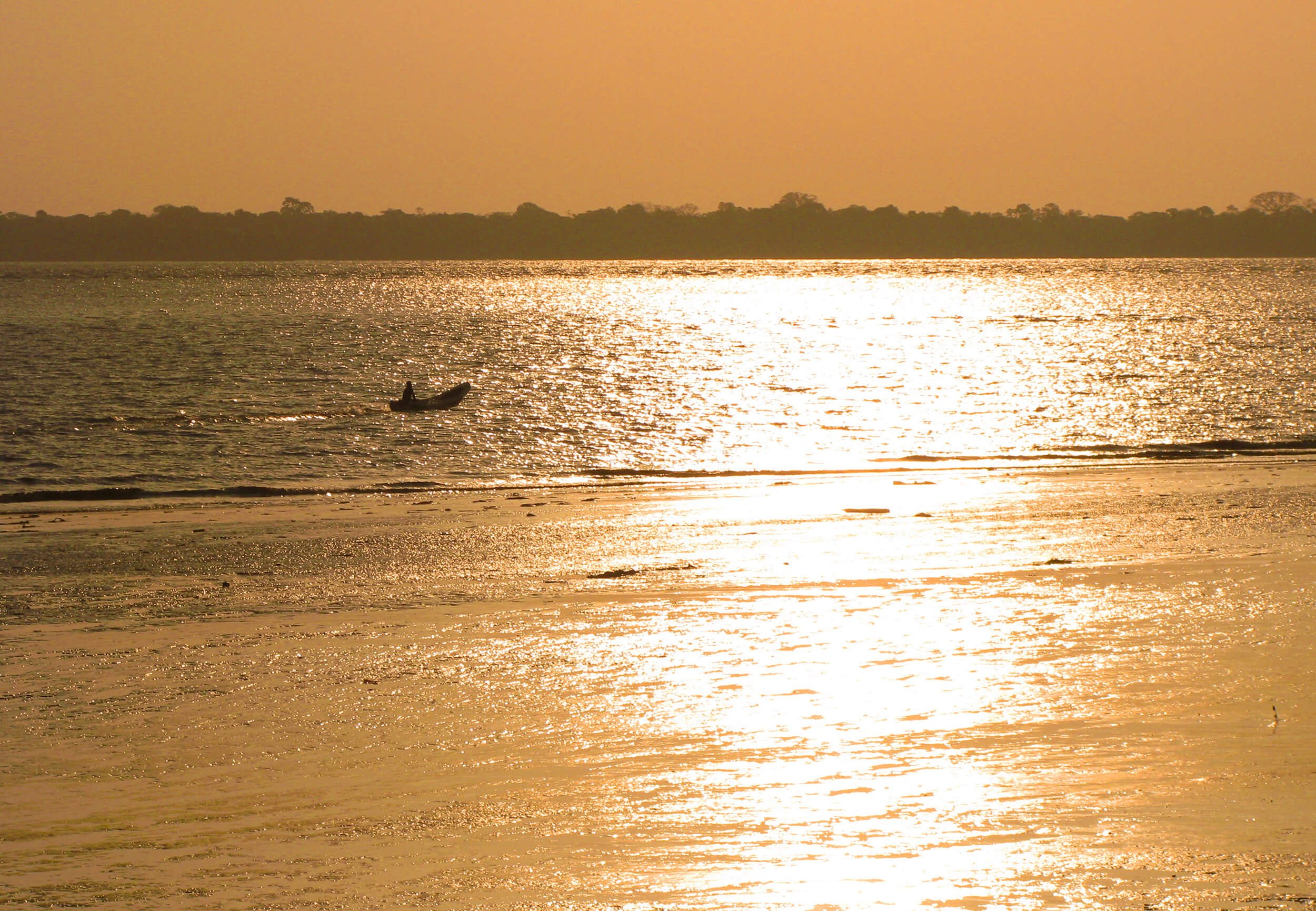 A person kayaking on a body of water during sunset, with the sky and water reflecting a golden hue, and a treeline in the background.