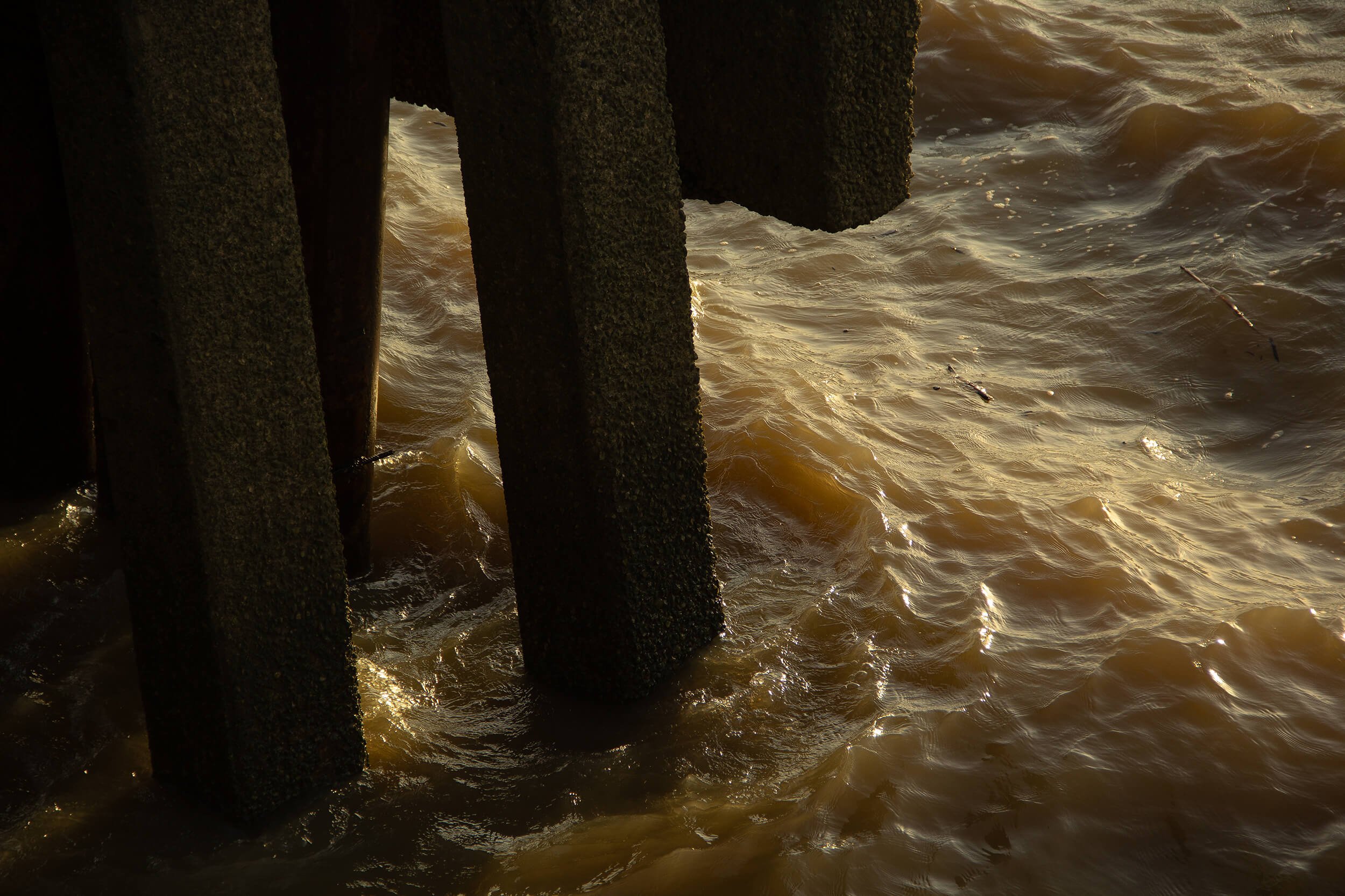 Water waves around wooden pilings at sunset.