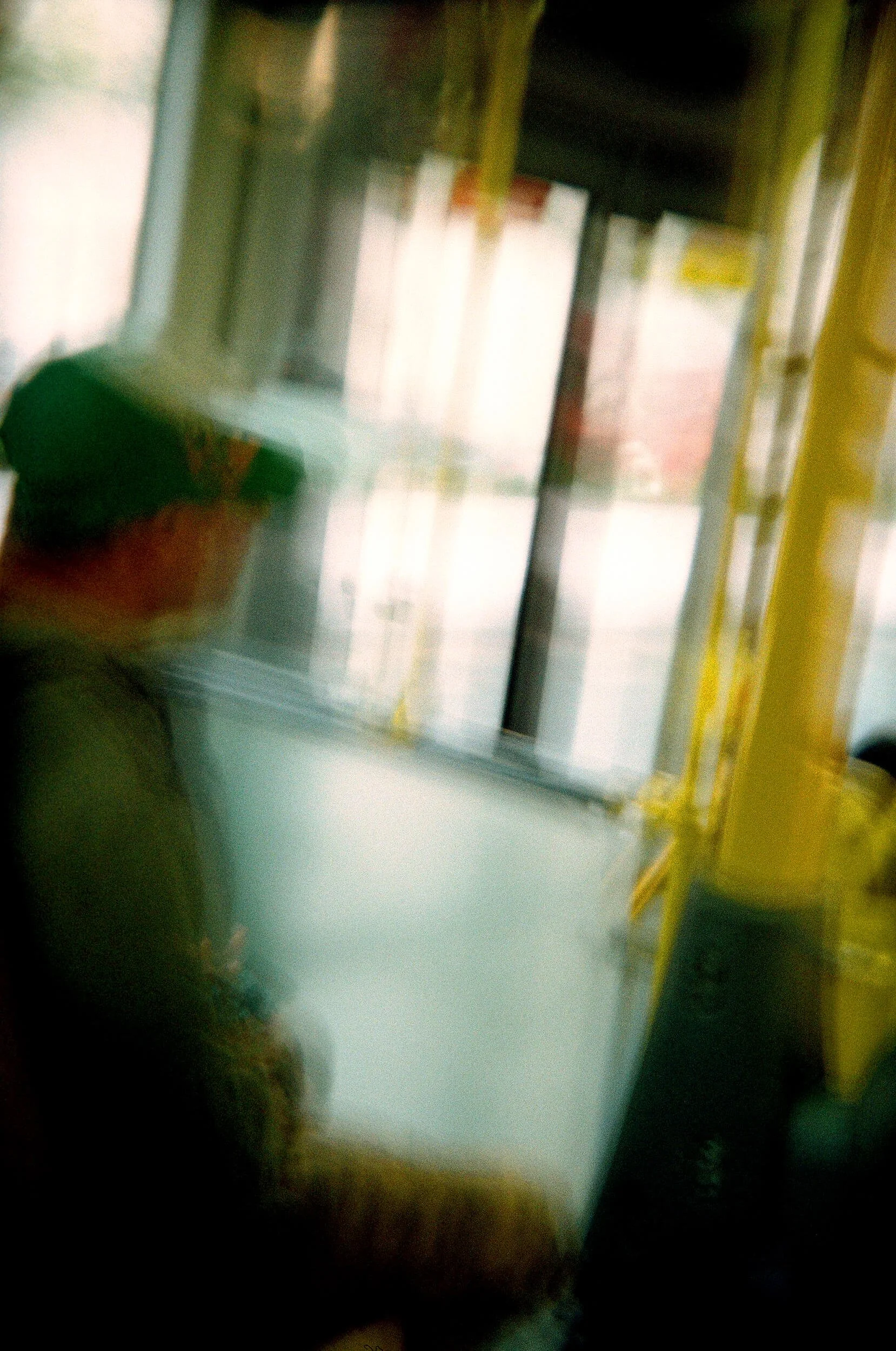 Blurred photo taken inside a public transportation vehicle, with yellow railing, windows, and passengers.