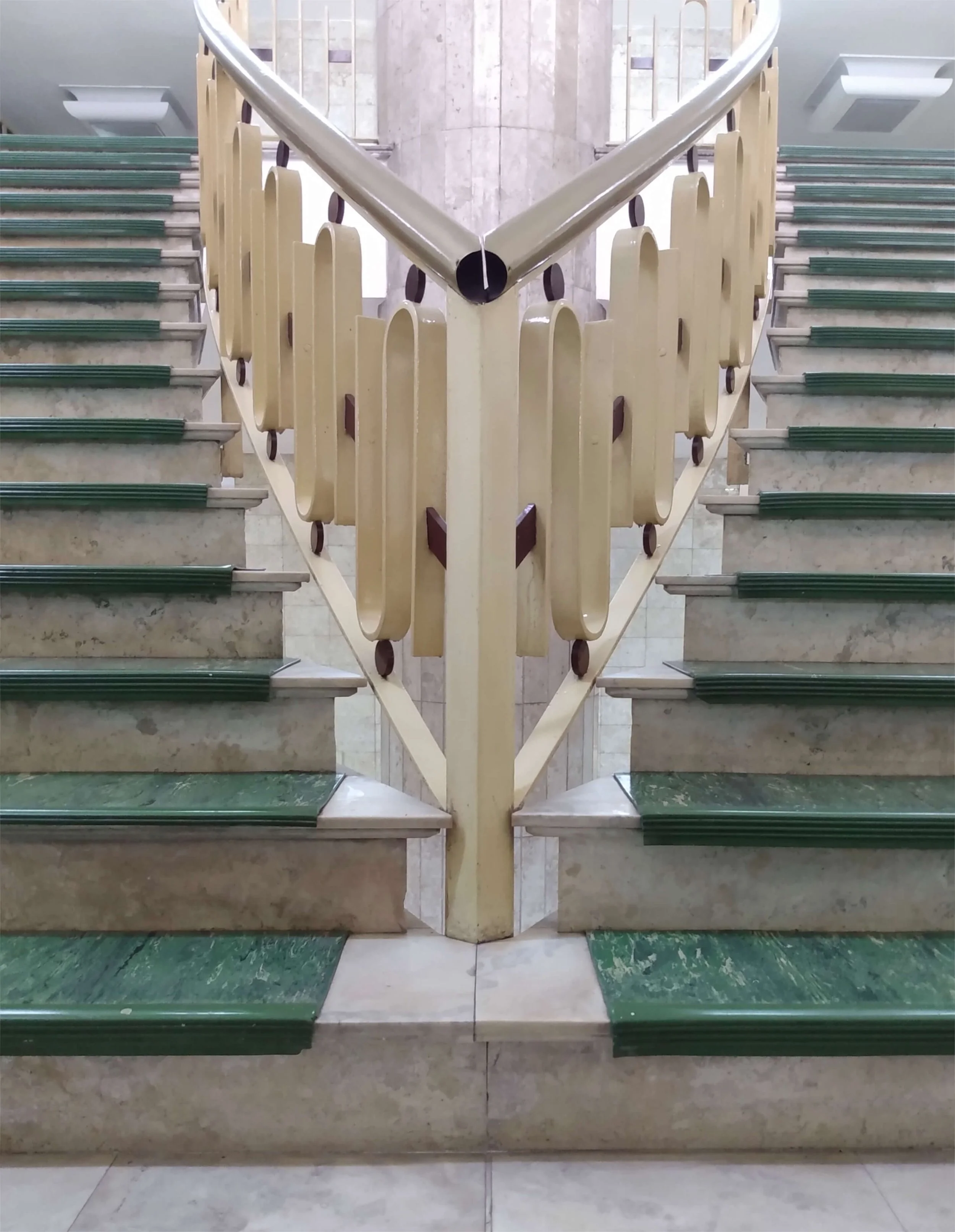Symmetrical staircase with green tread and beige railing, viewed from below, reflecting a mirror image.