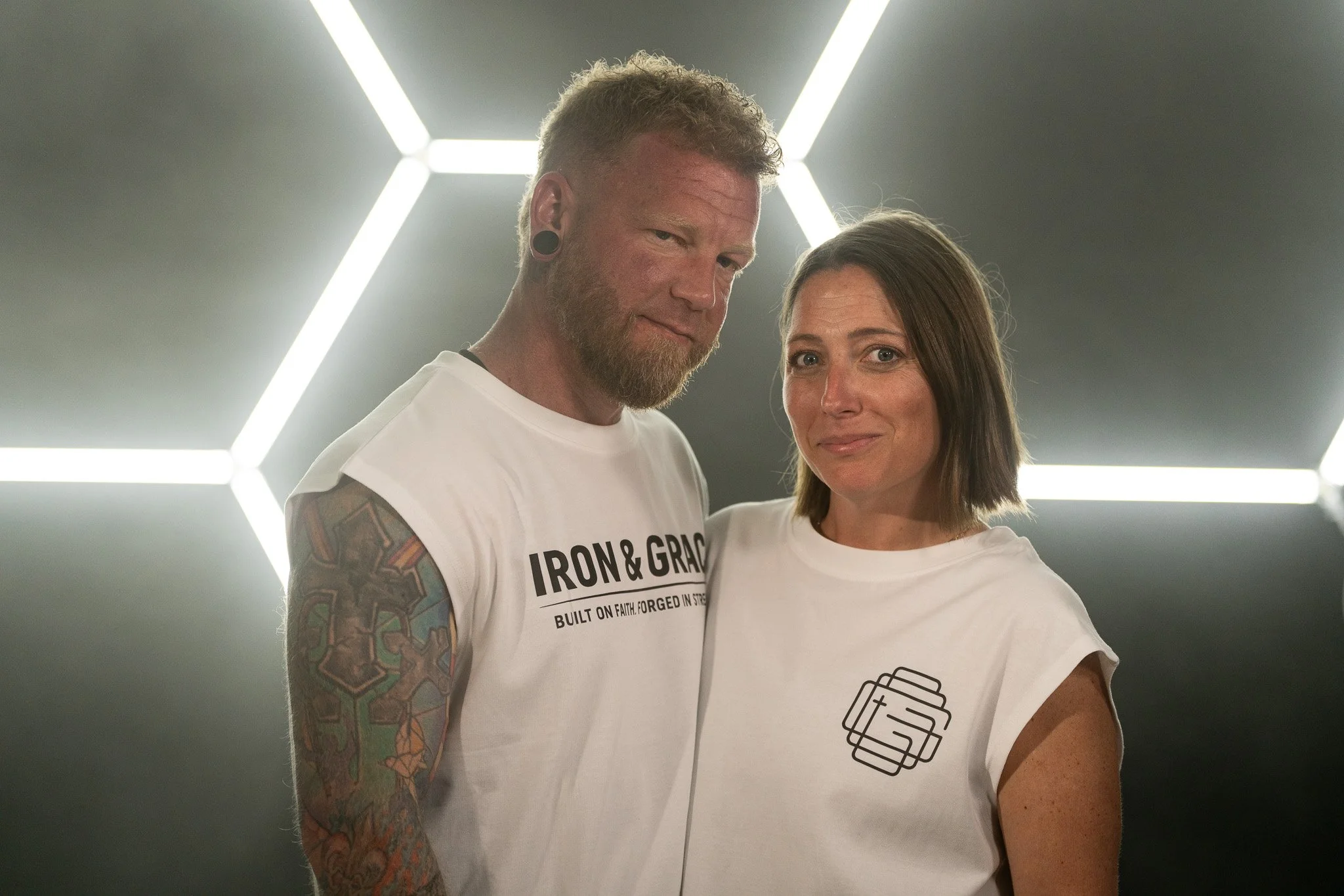 A man with tattoos on his arm and a woman standing inside a modern room with illuminated geometric ceiling lights.
