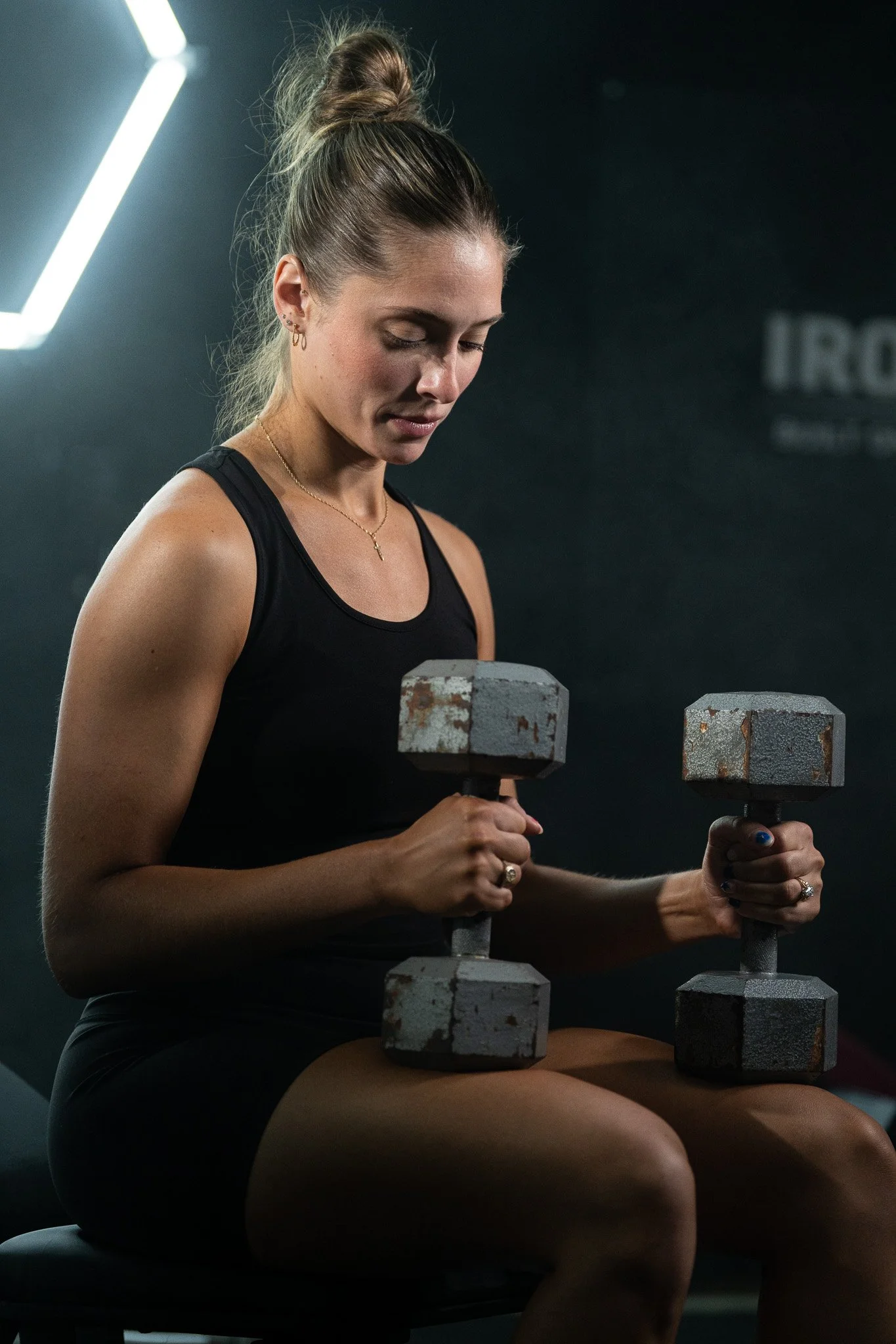 A woman sitting on a bench in a gym, holding dumbbells, focusing on her workout.