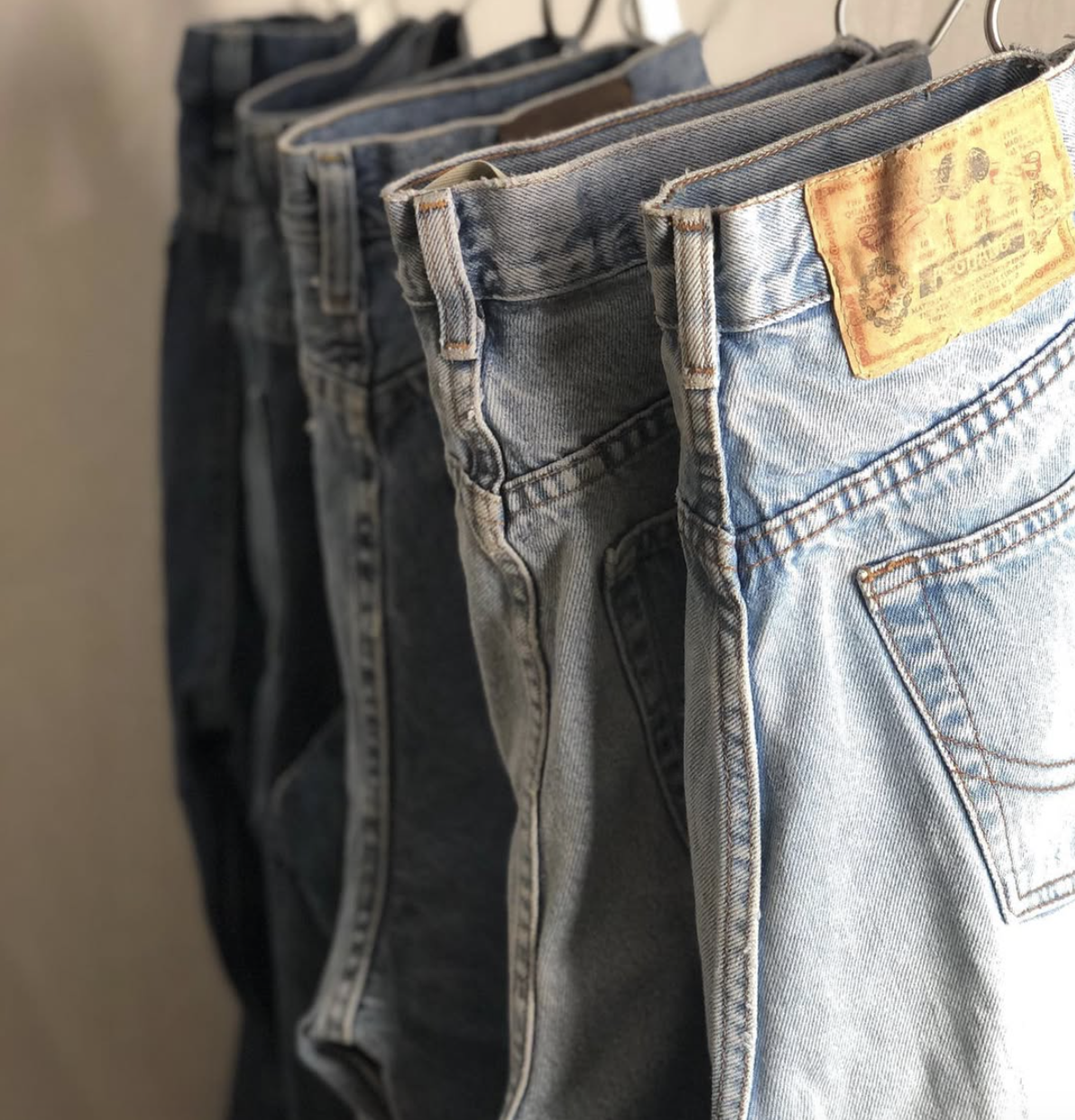 Three pairs of denim jeans hanging on hooks, varying in color from dark to light wash.