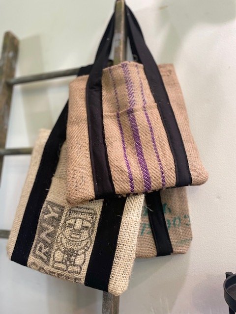 Several tote bags made from burlap hanging on a hook.