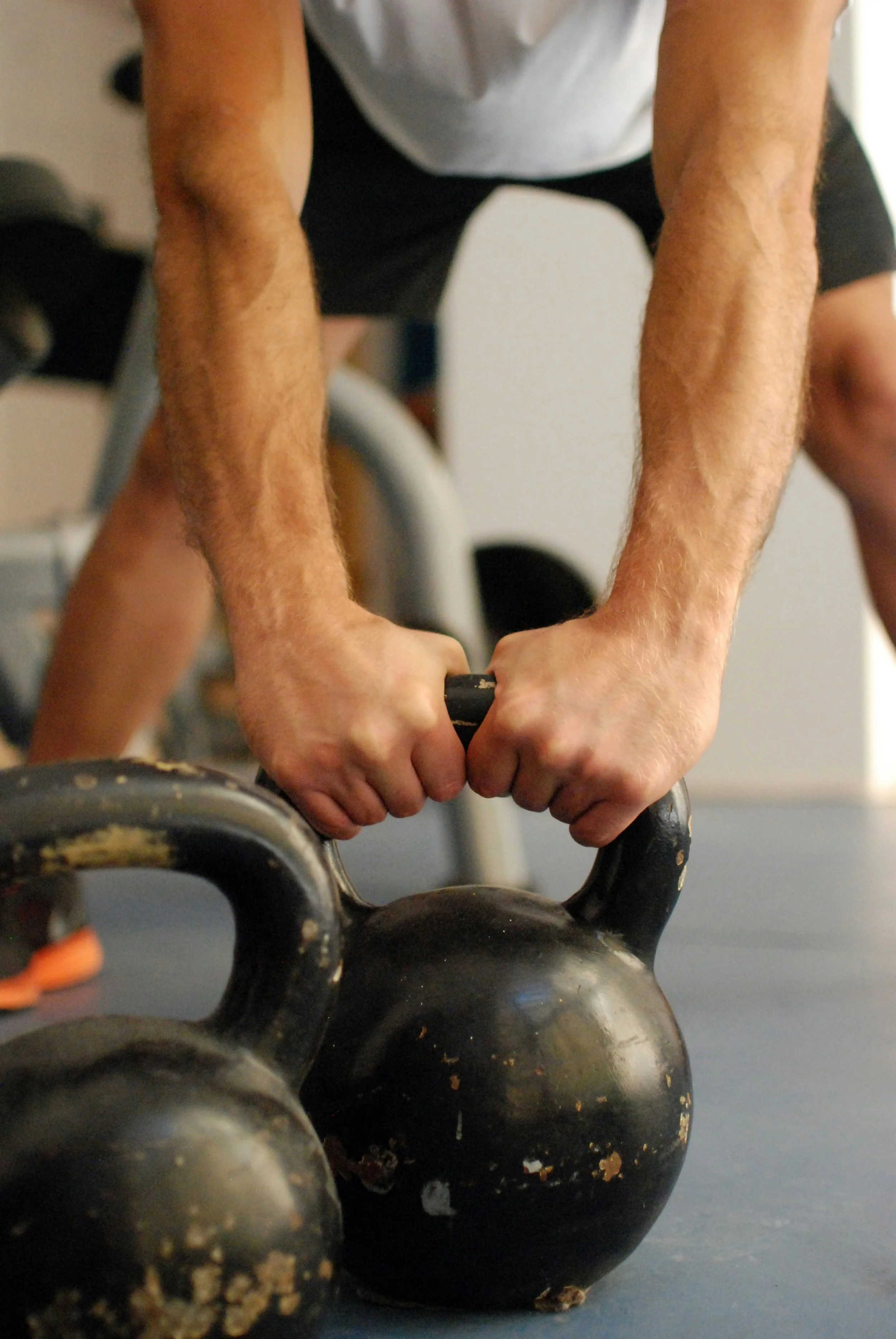 A person bending over and gripping the handles of a black kettlebell during a workout or exercise session.