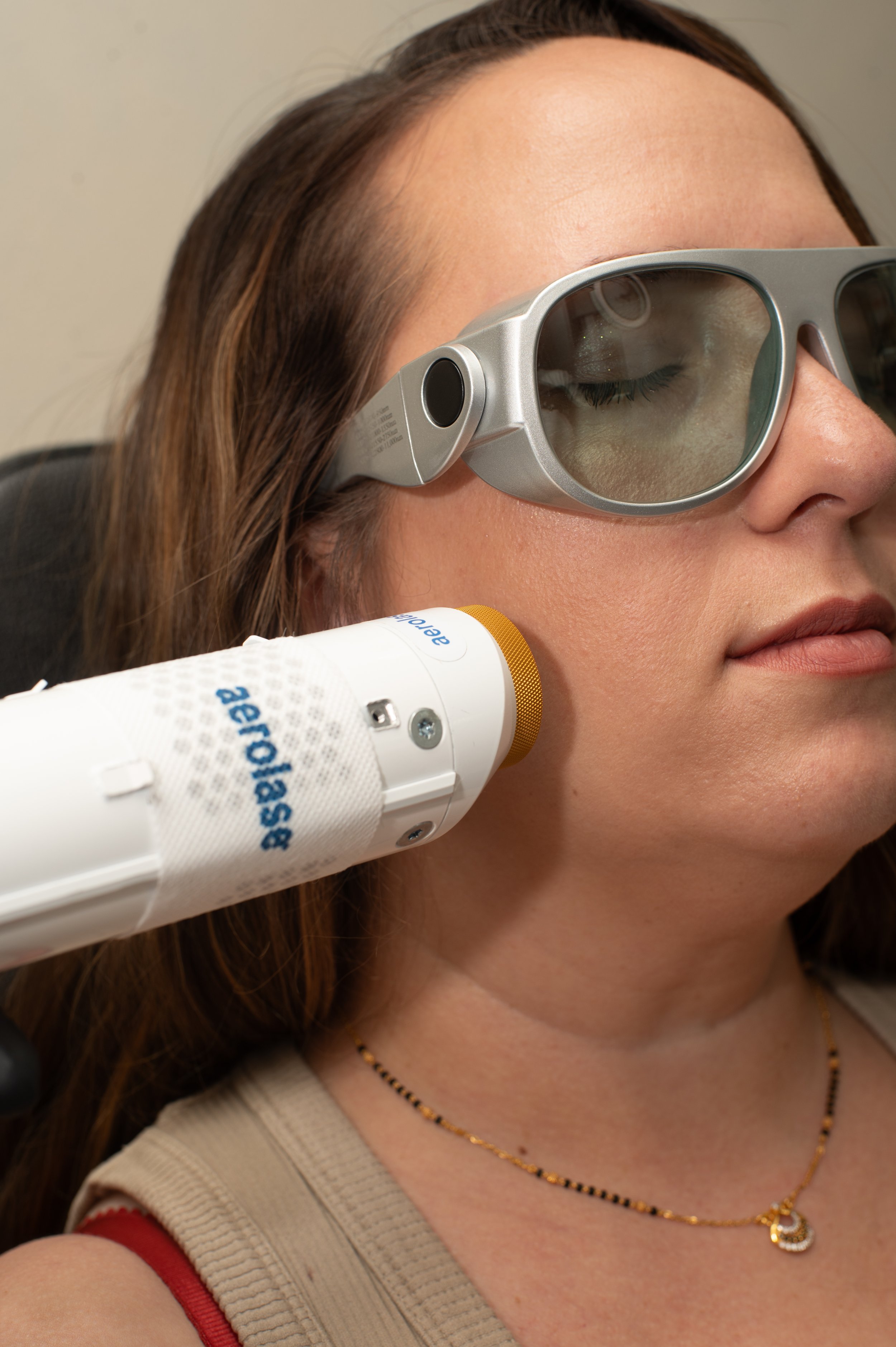 A woman wearing protective eyewear undergoes a dental or medical imaging procedure with a dental or medical device near her face.