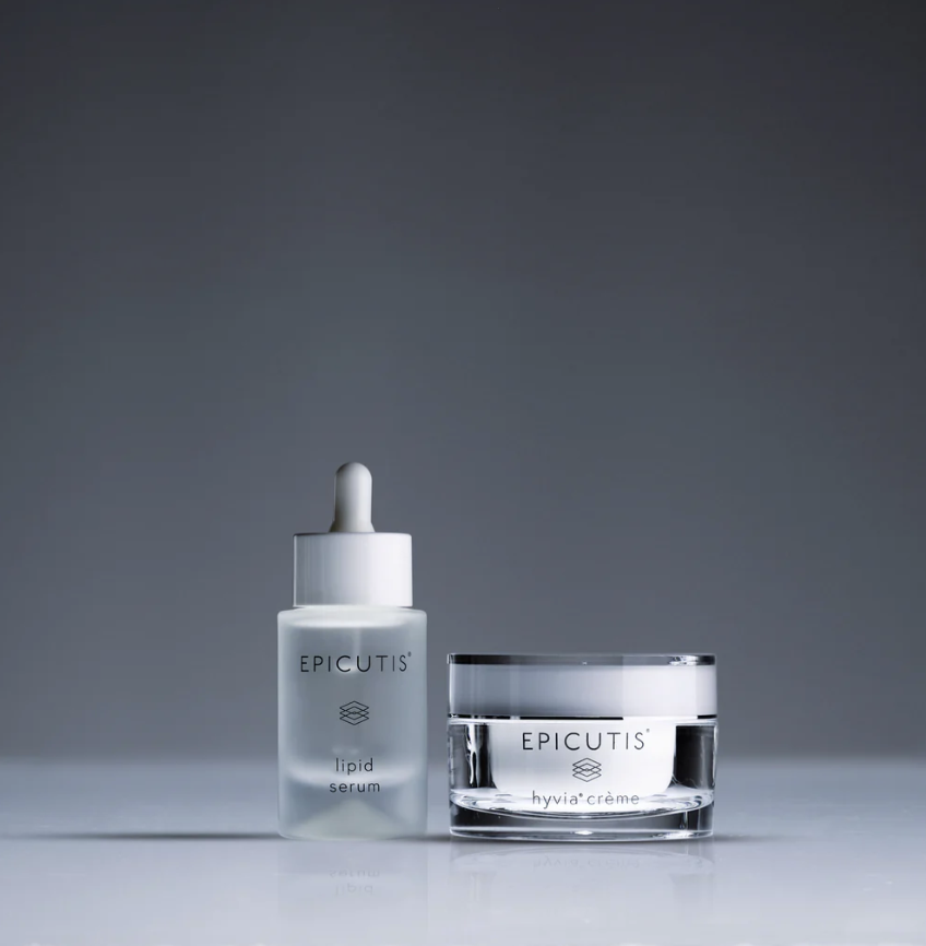 Two skincare products, a white dropper bottle labeled "lipid serum" and a clear jar labeled "hyvia crème," both from Epicutis, placed on a reflective surface against a gradient grey background.