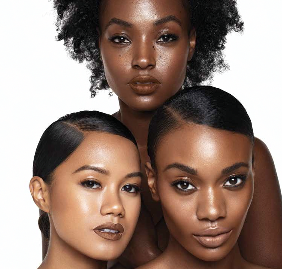 Portrait of three women with natural makeup and sleek hairstyles, posing against a plain white background.