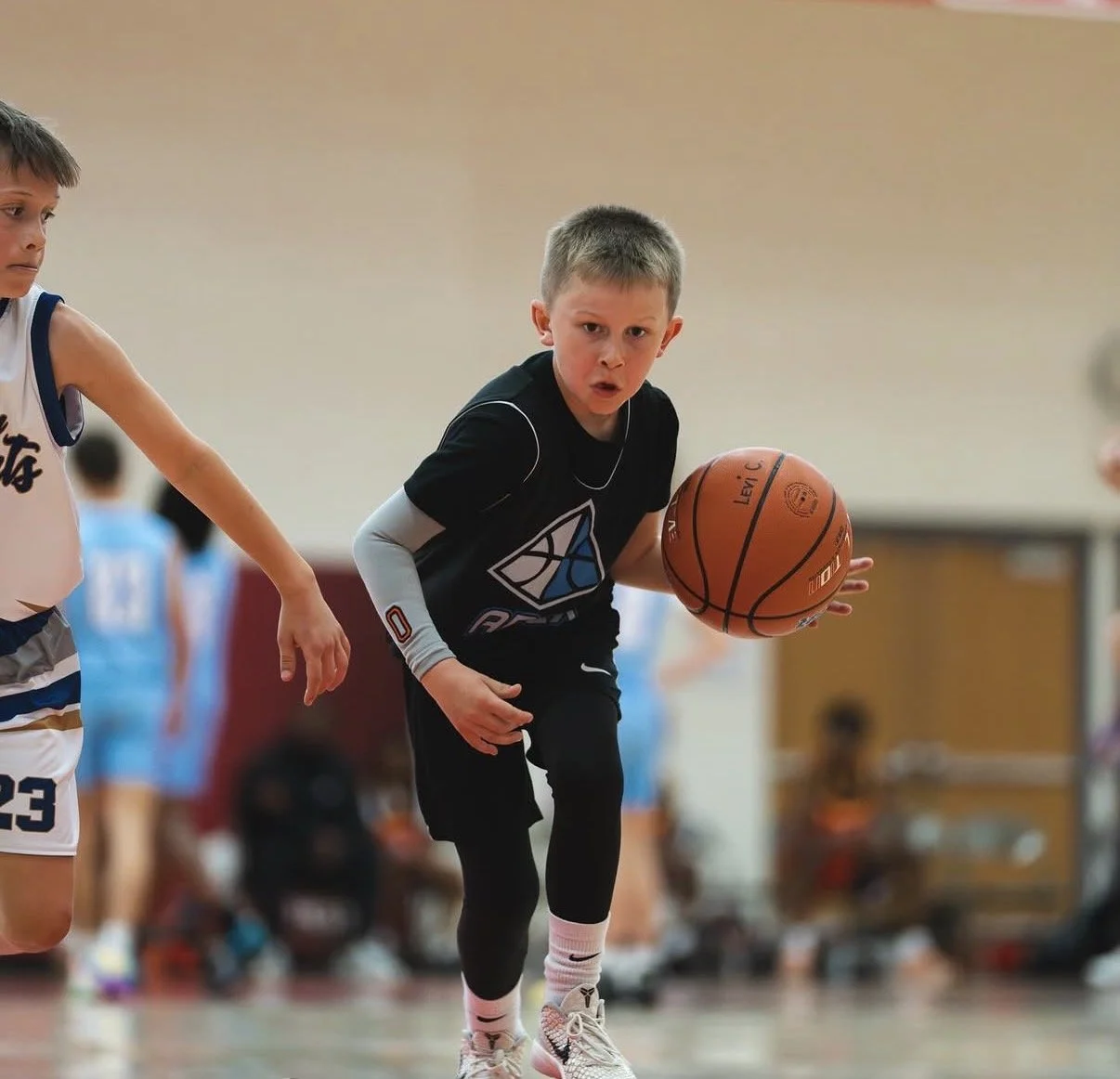 Young boy in black and white basketball uniform dribbling a basketball during a game in an indoor gymnasium.