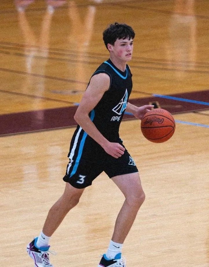 A young male basketball player dribbling a basketball on an indoor court, wearing a black and blue jersey with the number 3.