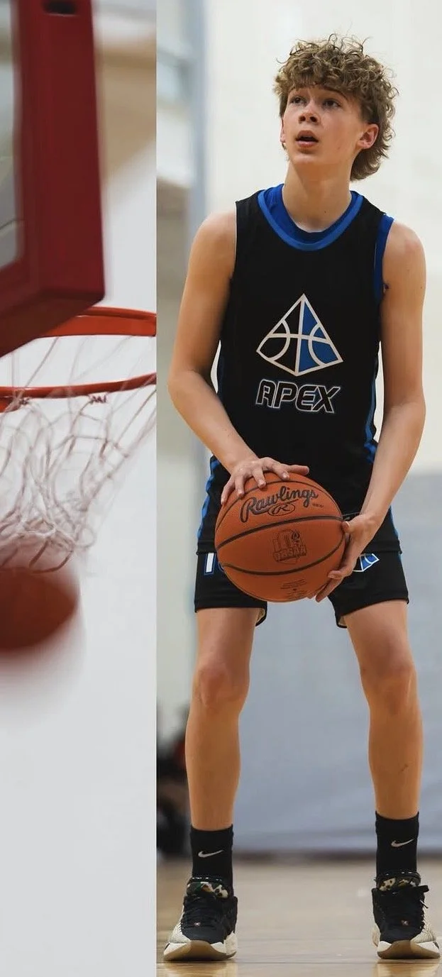 A young male basketball player with curly hair, wearing a black tank top with blue accents and a logo that says 'APEX', holding a basketball on an indoor court, preparing to make a shot.