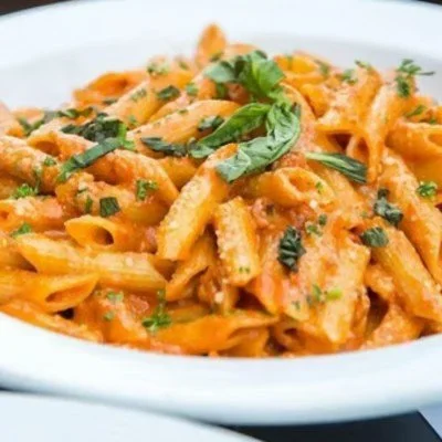 Pasta with tomato sauce, garnished with chopped herbs and a basil leaf.