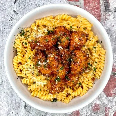 Bowl of rotini pasta topped with fried chicken pieces, Parmesan cheese, and chopped parsley.