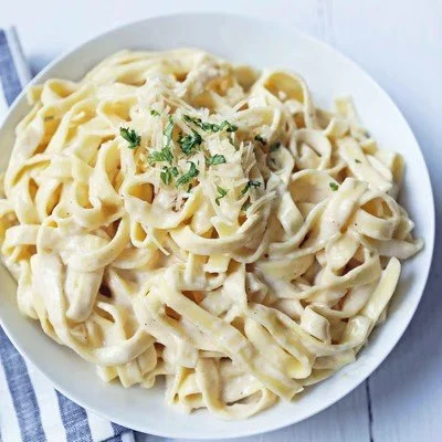 A bowl of fettuccine pasta with creamy sauce and chopped herbs.