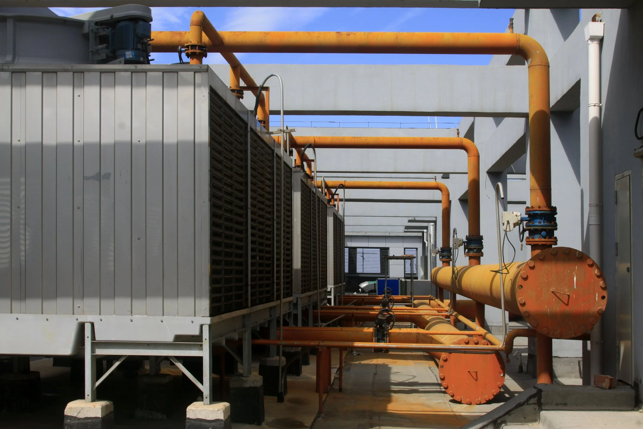 Industrial equipment with orange pipes and a large gray cooling unit on a rooftop against a blue sky.