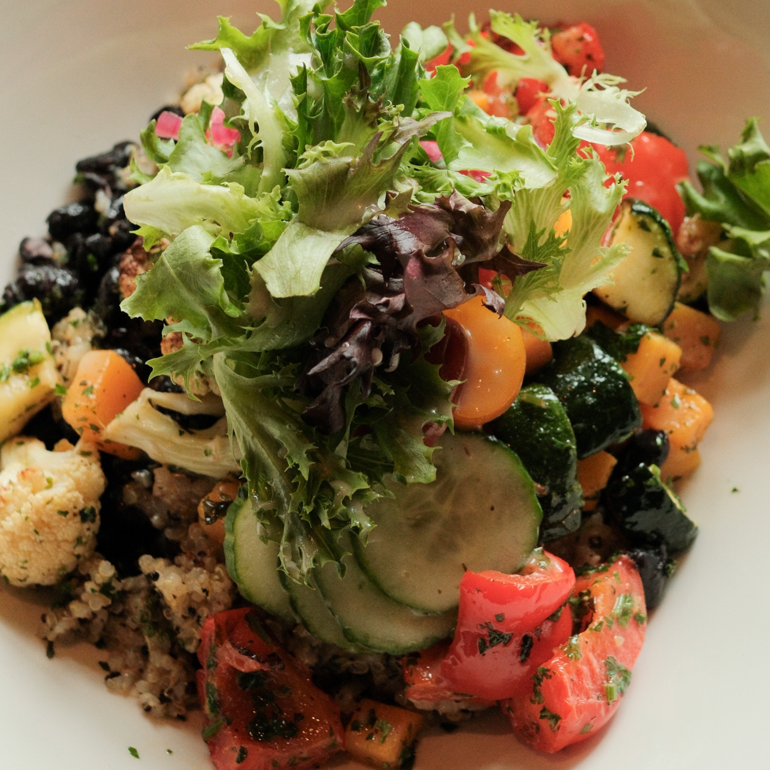 Fresh mixed vegetable salad with leafy greens, cucumber slices, cherry tomatoes, zucchini, cauliflower, and shredded carrots.