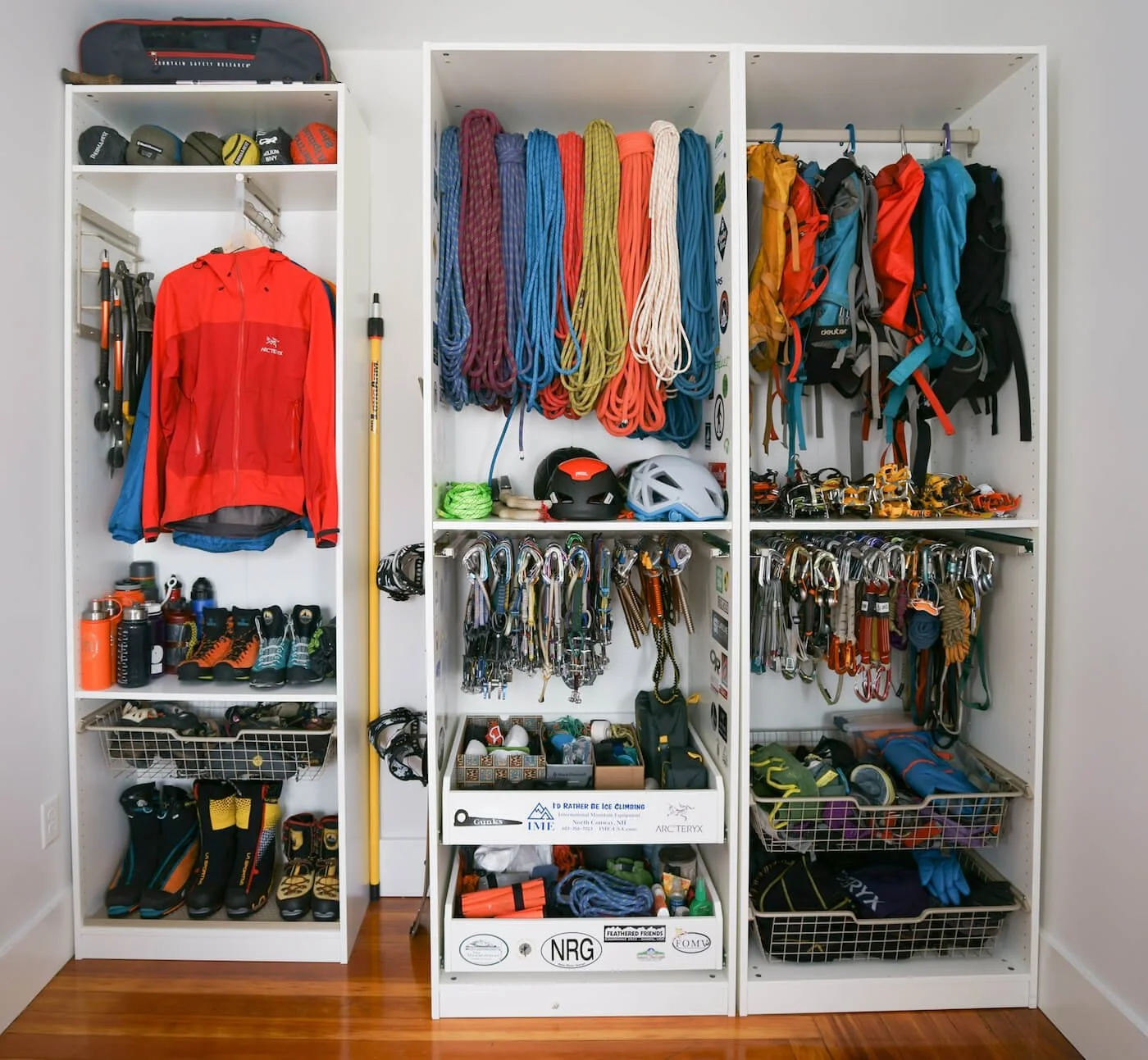 Organized climbing gear and accessories in white shelving units, including ropes, helmets, harnesses, shoes, water bottles, and apparel.
