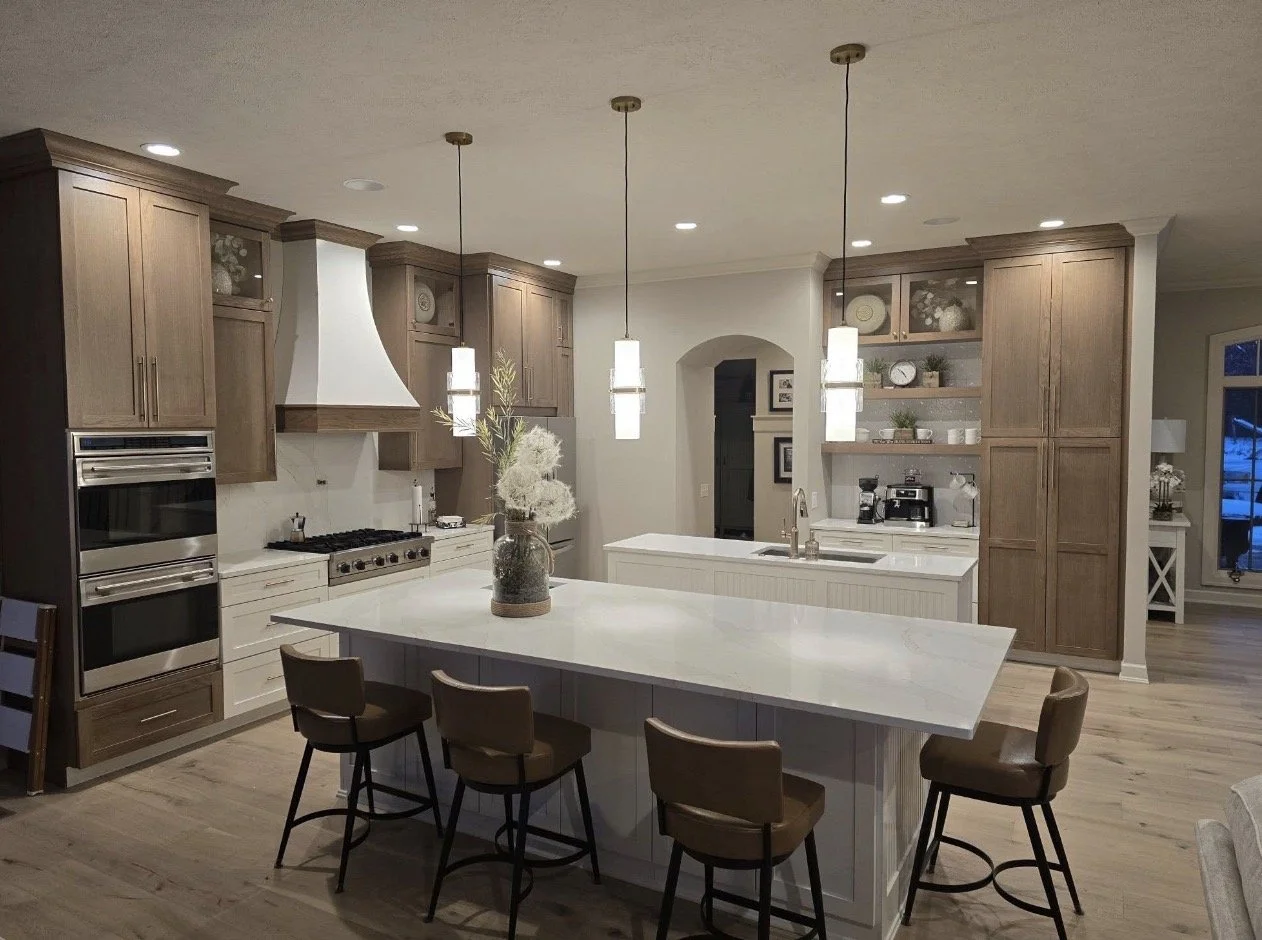 Modern kitchen with island, pendant lights, hardwood floors, wooden cabinets, and built-in ovens.
