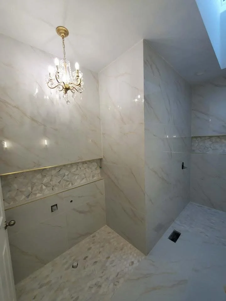 A bathroom under construction or renovation with marble tiles and a chandelier hanging from the ceiling.