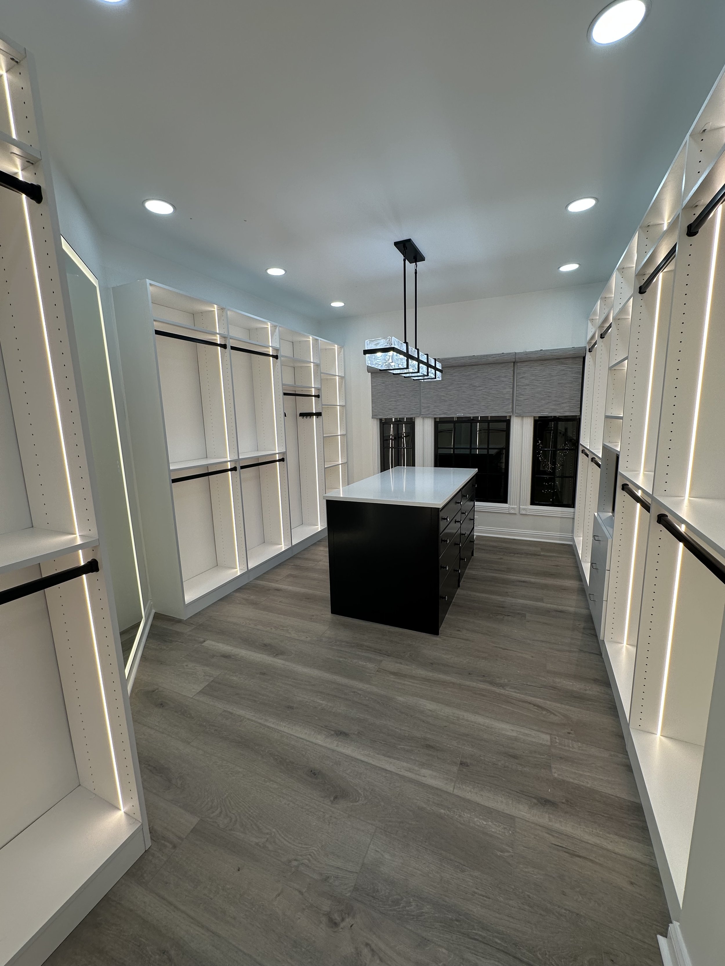 Empty walk-in closet with white shelves, black clothing rods, a central black island, and modern ceiling lights.
