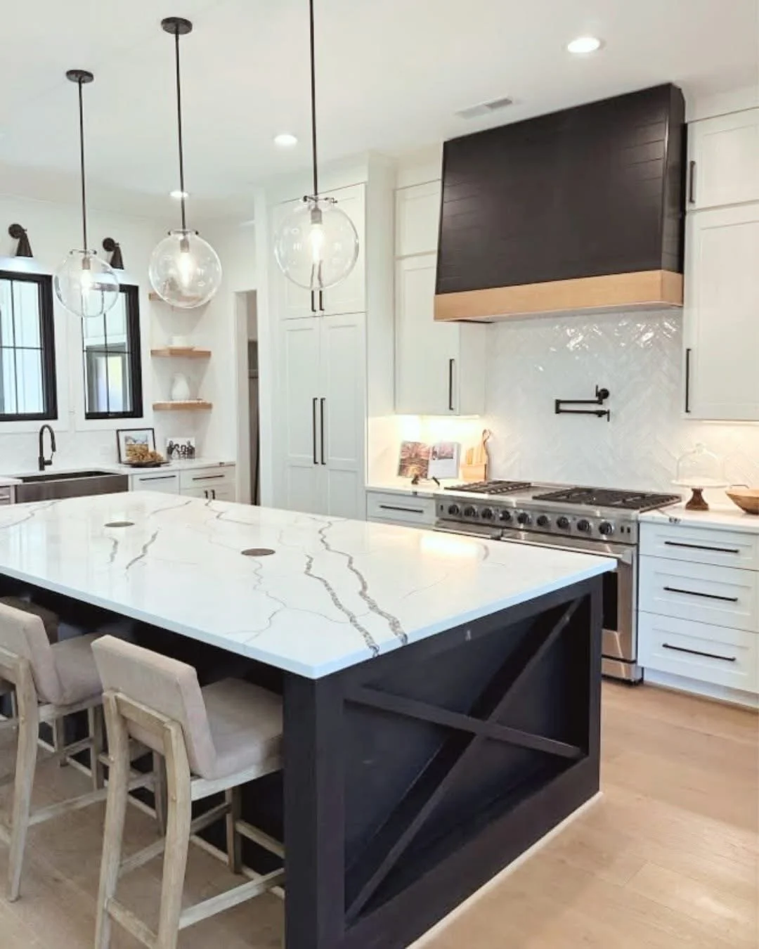 Modern kitchen with white cabinetry, a large marble island with dark base, pendant lights, and stainless steel appliances.