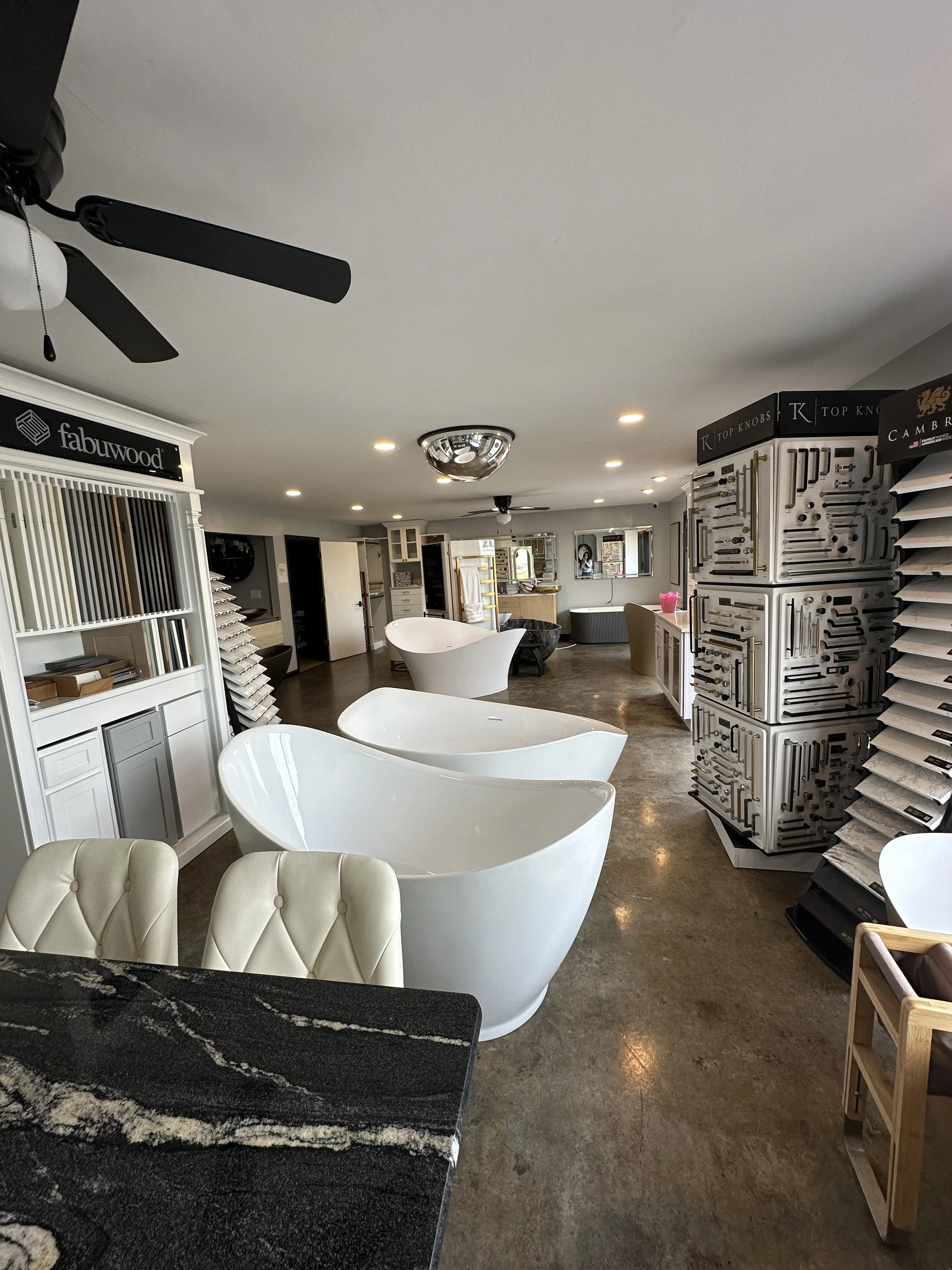 Interior of a furniture store with display samples, including white bathtubs, a black and beige rug, and various furniture pieces and cabinet hardware displays.
