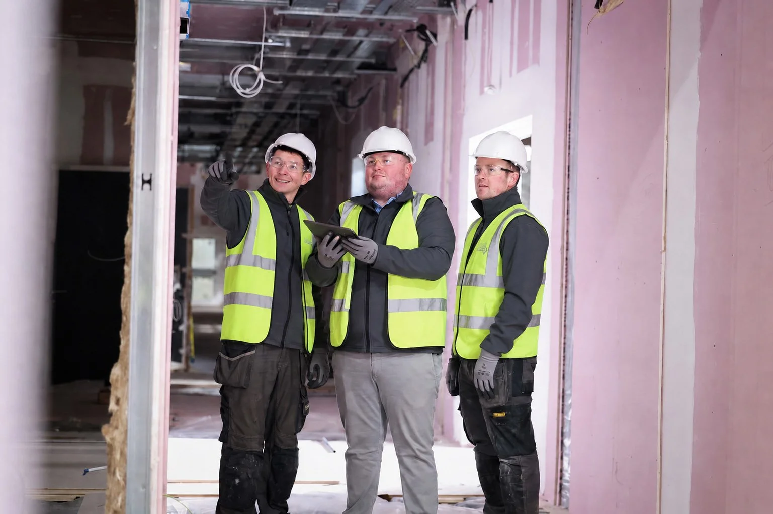 Three construction workers in safety vests and helmets inspecting a building under construction.