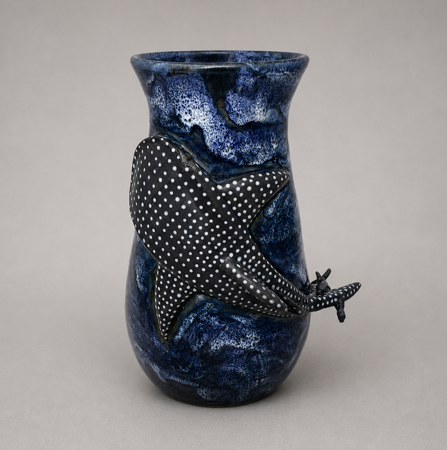 A blue marbled ceramic vase with a black and white polka dot sculpted salamander attached to its side.