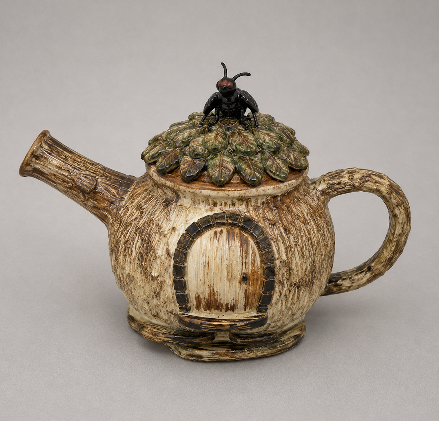 A teapot designed to resemble a tree trunk with a handle, spout, and small door, topped with a miniature black spider figurine on a bed of leaves.