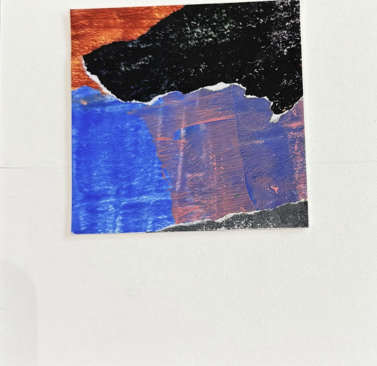 A torn piece of artwork or paper with abstract paint in black, orange, purple, and blue colors, mounted on a white wall.