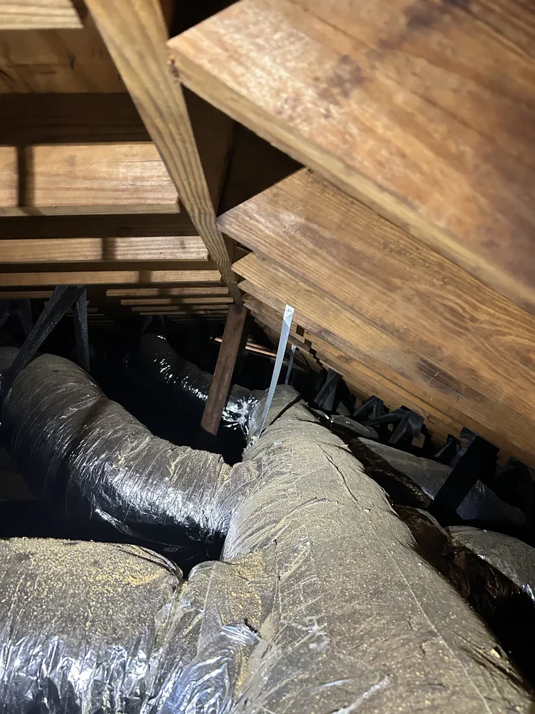 Attic with exposed wooden beams, ductwork wrapped in insulation, and a metal support pole.