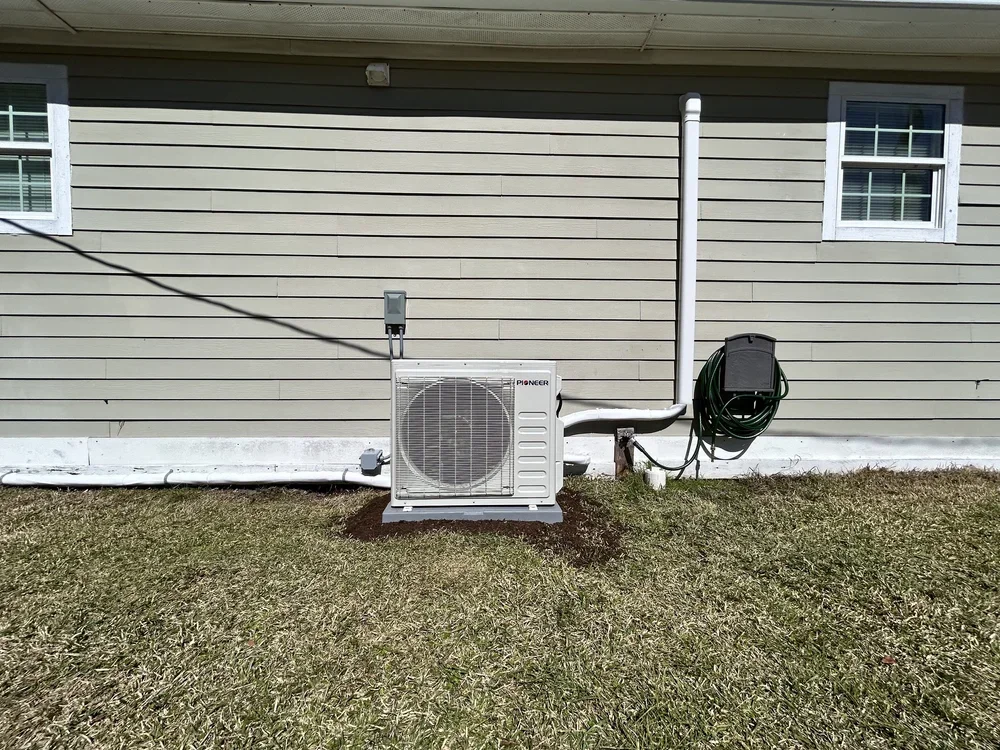 Exterior view of a house with a Pioneer air conditioning unit, electrical box, garden hose reel, and a white gutter system.