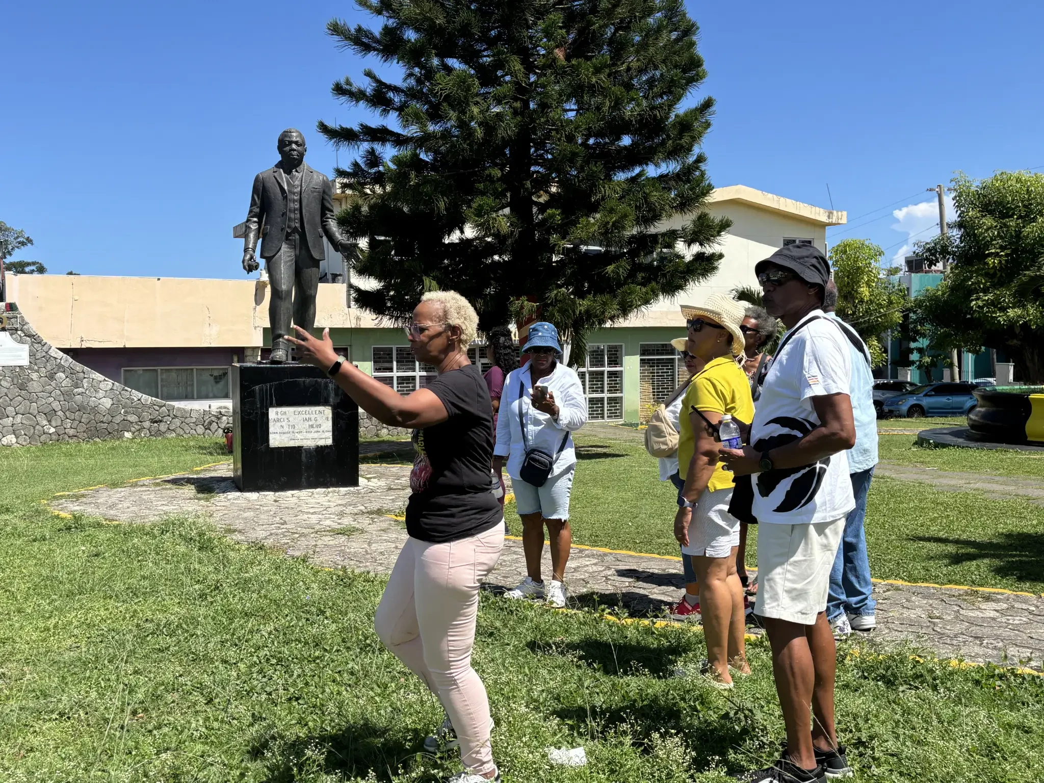Tour guide gesturing toward a bronze statue of Marcus Garvey