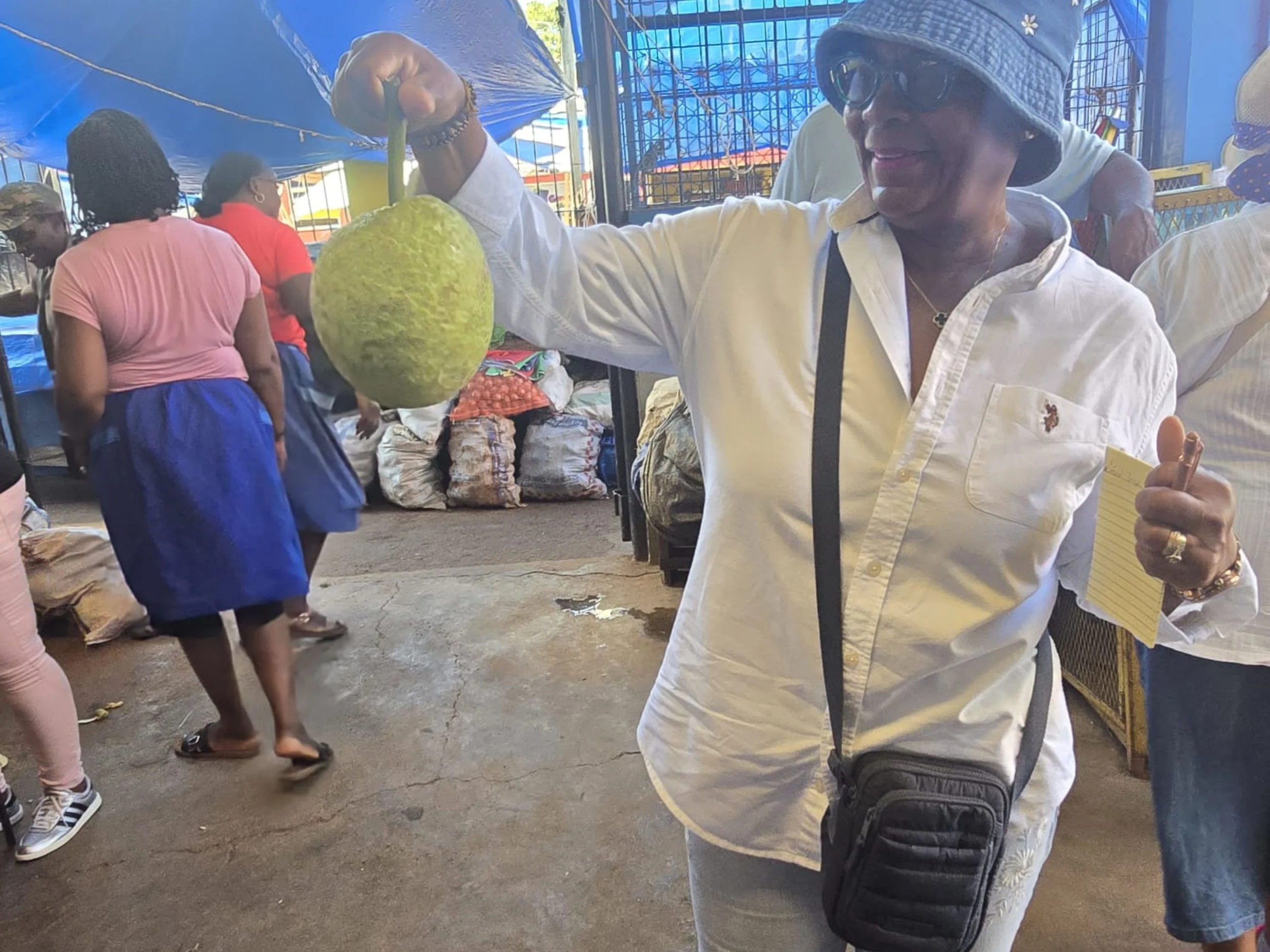 Woman smiling while browsing a busy outdoor market with vendors selling produce and goods in the background.