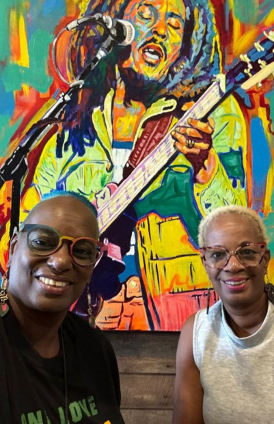 Anne and Janet Crick, Owners of Jamaica Culinary Tours, posing in front of a colorful mural depicting Bob Marley  playing guitar.