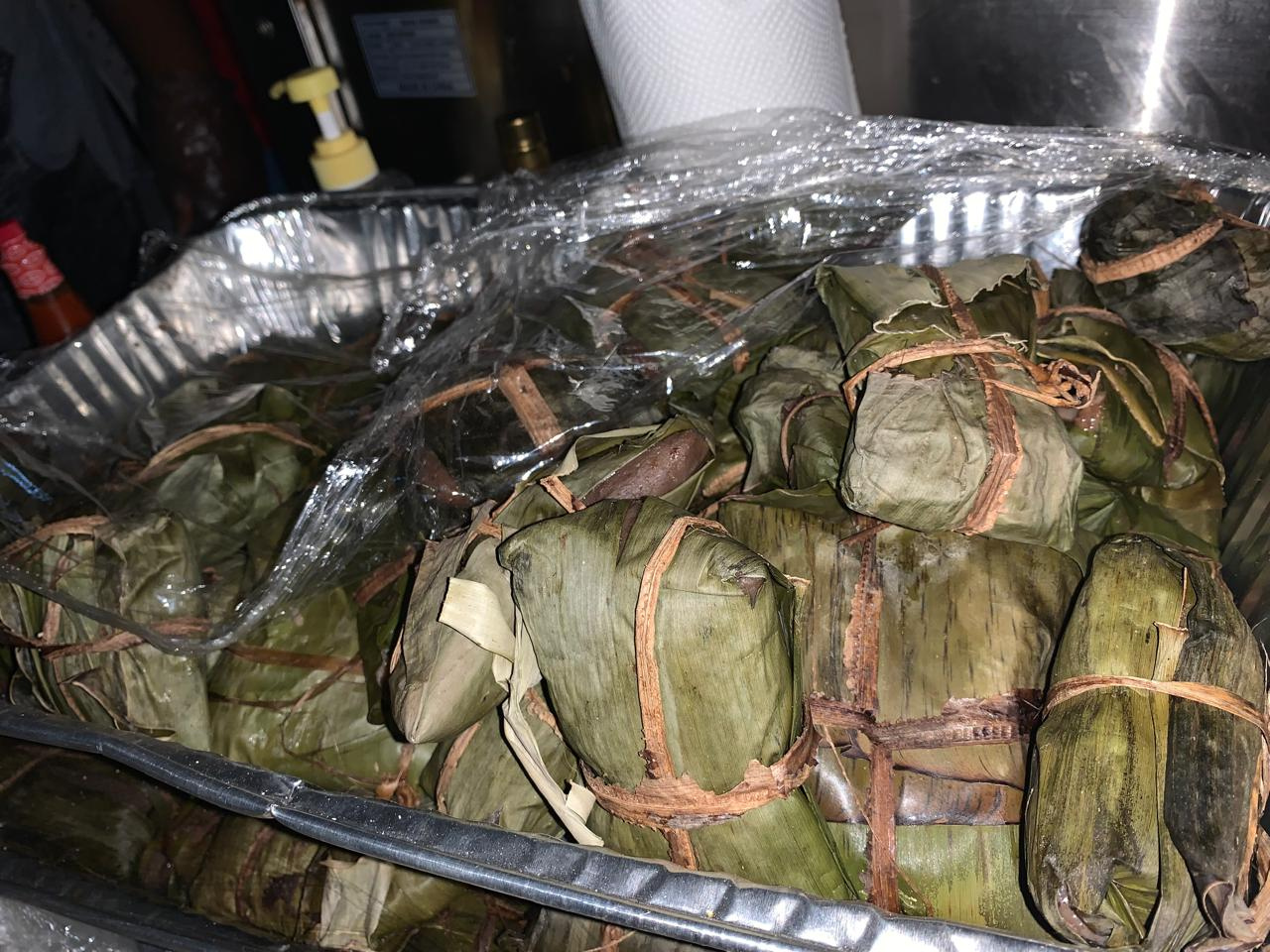 A rectangular aluminum foil pan packed with fresh Jamaican Dukanoo, showcasing its rich, dense texture and dark brown color.