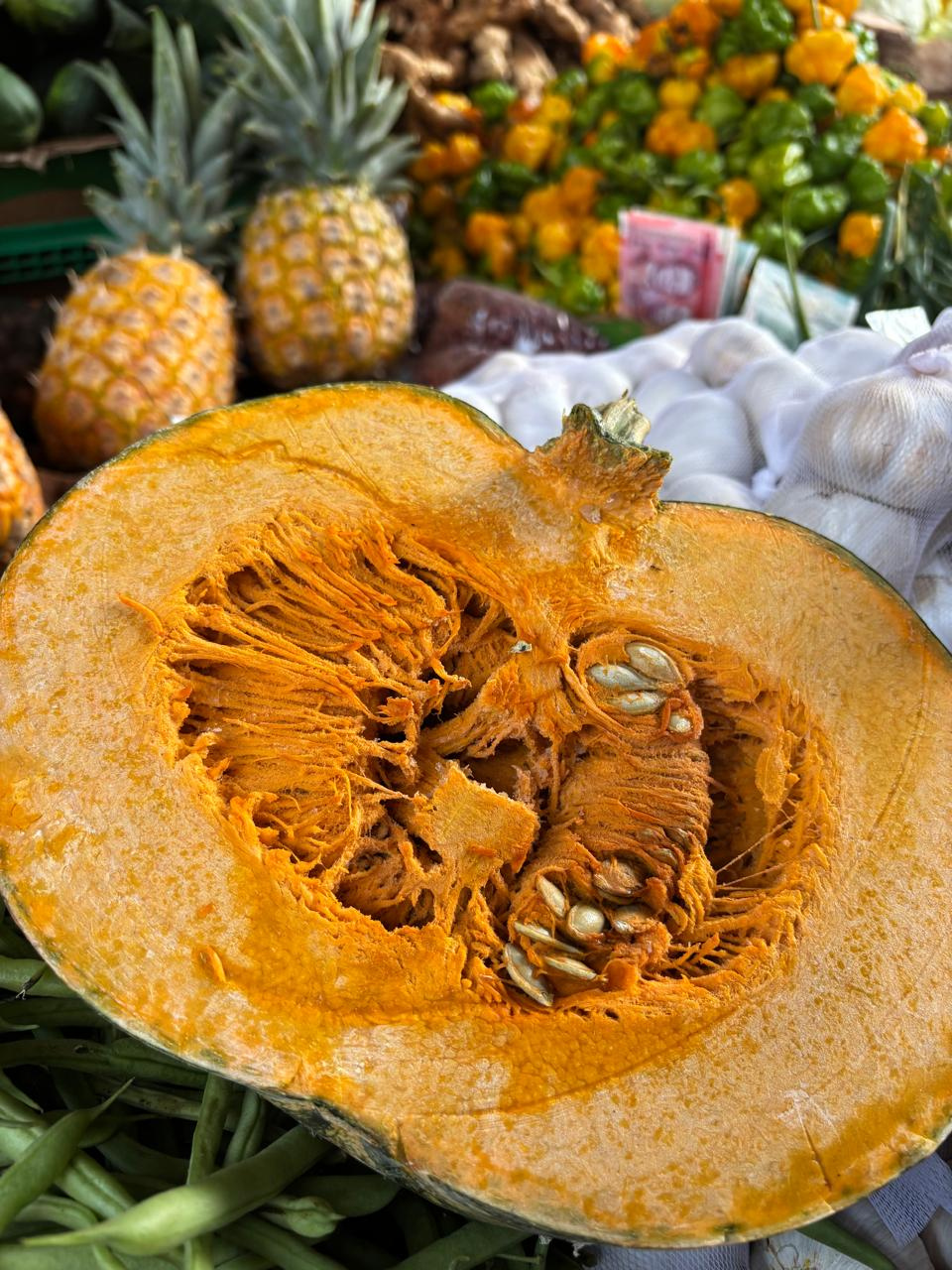 Marketplace close up of pumpkin , pineapple to the side and stocks of garlic behind the pumpkin