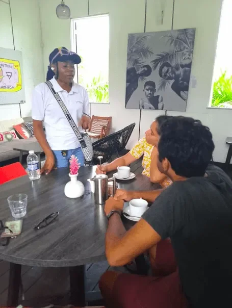 Jamaica Culinary Tours guide presenting a local coffee tasting experience to international travelers seated at a café table on the Roots & Routes excursion.