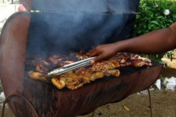 Chicken pieces being jerked on a grill inside a traditional Jamaican drum pan.