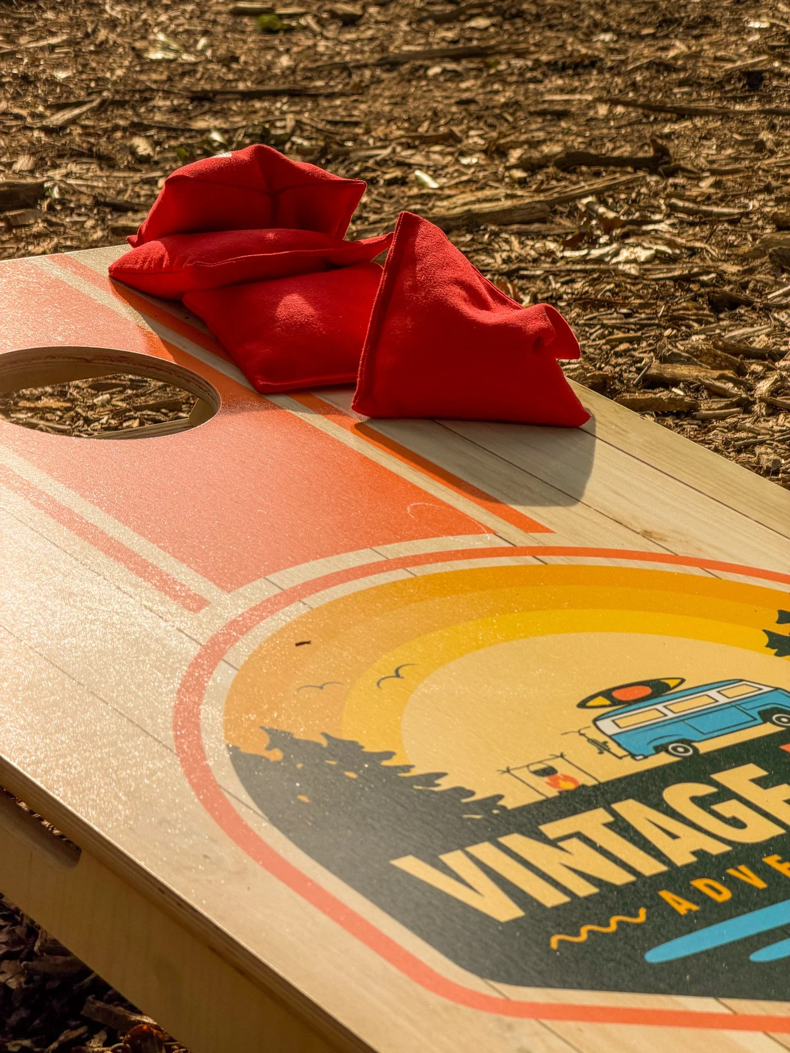 A close-up of a shuffleboard court with red shuffleboard pucks on the playing surface, illuminated by sunlight.