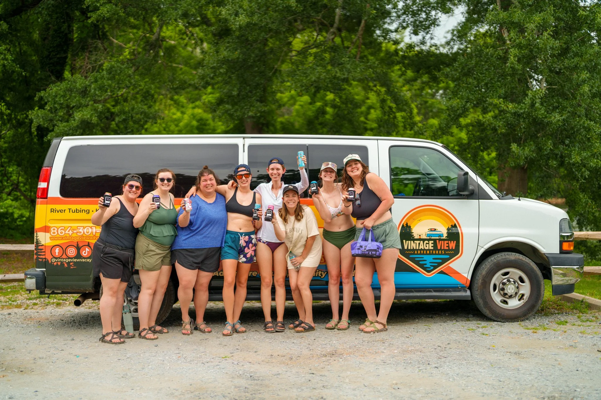 A group of nine women in casual summer clothing standing in front of a van with a colorful 
