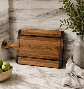 Wooden cutting board leaning against a marble countertop, with a potted plant and a bowl of green apples nearby.