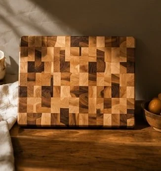 A wooden cutting board with a geometric mosaic pattern, placed on a wooden surface with a bowl of apples nearby.