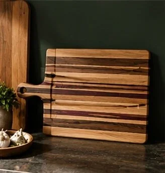 Wooden cutting board with striped pattern leaning against a wall on a dark countertop.