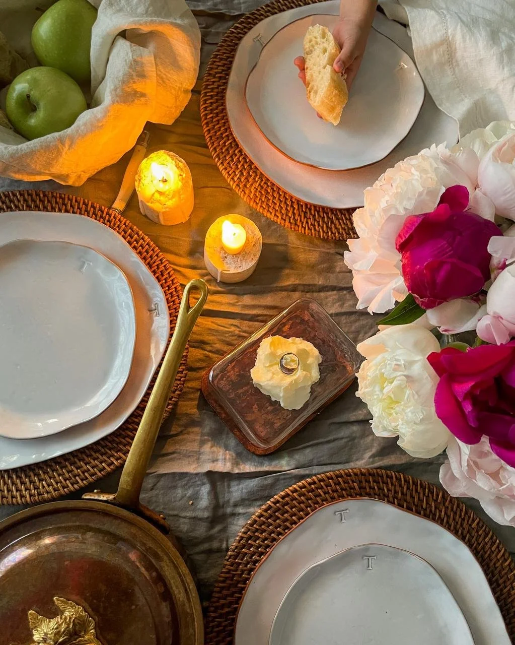 Candlelit dinner table with rattan chargers, peonies, copper pan and linen — At Home With Elena